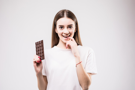 Sensual image Sensual image of a beautiful young woman biting a bar of milky chocolate playfull look on camera before eat isolated on grayの写真素材