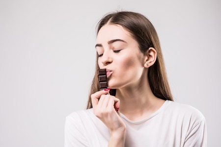 Portrait of beautiful smiling woman enjoy eating chocolate isolated on gray background.の写真素材