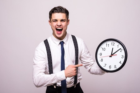 Screaming man in business clothes holding and pointing at clock over white