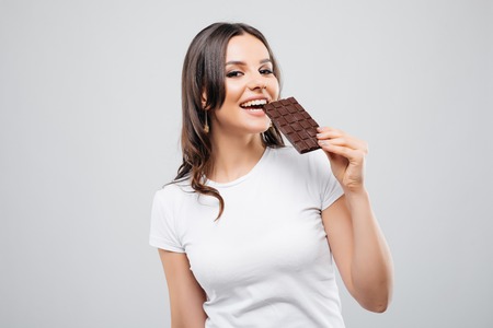 portrait of a brunette young woman biting chocolate isolated on whiteの写真素材