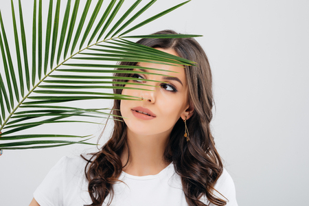 Beauty portrait of a smiling woman with brunette hair posing with green leaves over white backgroundの写真素材