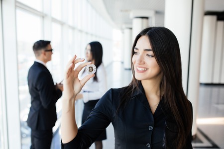 Blockchain and investment concept. Business woman leader holding bitcoin in front of his discussing team on office.の写真素材