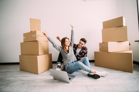 Young couple sitting on the floor happy with raised hands looking on laptop after moving in new...