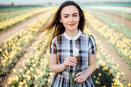 Beautiful woman with white tulip in hands in tulips fieldの写真素材