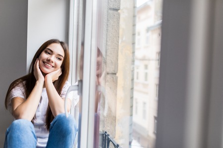 Beautiful smiling woman sitting on windowsill and smileの写真素材