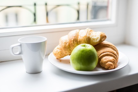 Composition with tasty breakfast apple and croissant on windowsillの写真素材