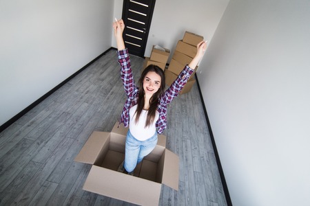 Young woman sitting inside cardbox with raised hands after moving in new hauseの写真素材