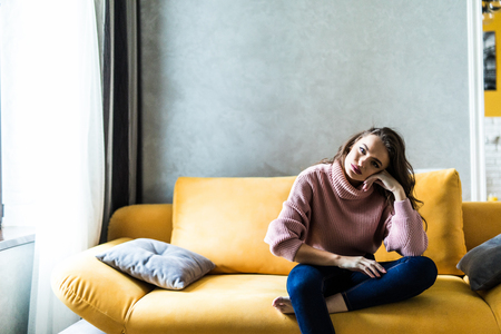 Picture of a tired unkempt woman lying on he couch at home. Girl watch TV new serial. Sofa relax concept after hard working day. Attentive female in blue jeans and t-shirt watch cooking channelの写真素材