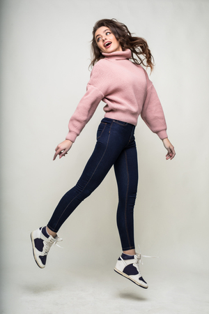 Full length portrait of a casual young woman jumping and looking at camera isolated over whiteの写真素材