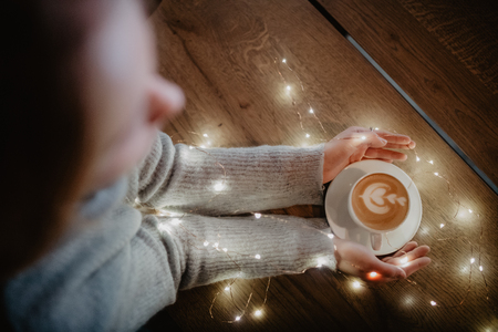 Girl holding coffee in hands over light bokeh background. Overhead shot.の写真素材