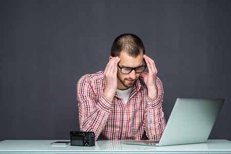 Pensive sad man sitting at the table with laptop over grayの写真素材