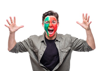 Handsome man supporter fan of Portugal national team painted flag face get happy victory screaming into a camera.の写真素材