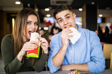 Cheerful Couple In Fast Food Reastaurant Eating Burgersの写真素材