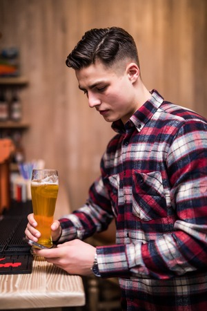 Young man with beer bottle using phone at counter in restaurant
