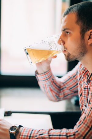 Man drinking beer. Side view of handsome young man drinking beer while sitting at the barの写真素材