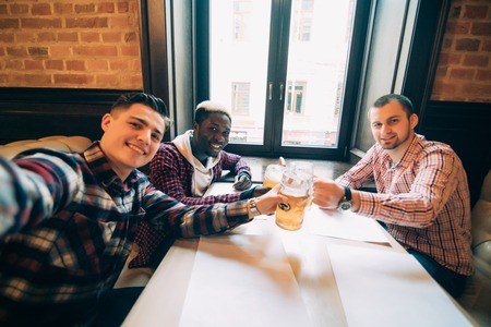 Cheerful old friends having fun by taking selfie and drinking draft beer in pub