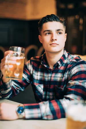 Man in beer pub. Cheerful young man holding a beer mug and smiling while sitting in bar