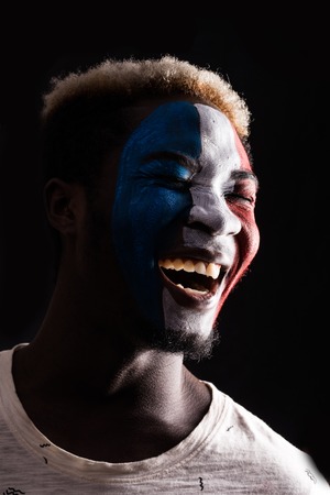Face portrait of happy afro fan support France national team with painted face isolated on darkの写真素材
