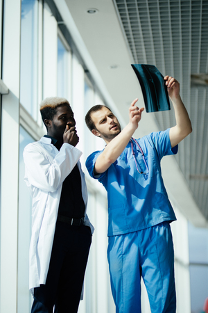 two male doctors reviewing x-ray in hospital corridorの写真素材