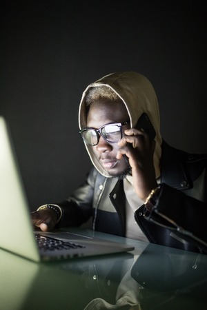 Young afro american man with laptop and cell phone at nightの写真素材