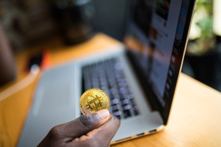 African Man holding in hand symbol of bitcoin crypto currency - electronic virtual money for web banking on laptopの写真素材