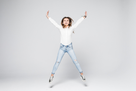 Full length portrait of a young beautiful brunette girl jumping and smiling happily isolated on white backgroundの写真素材