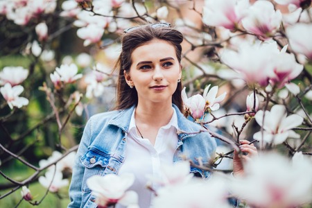 Sweet girl standing on soft background Magnolia blossoming flowersの写真素材