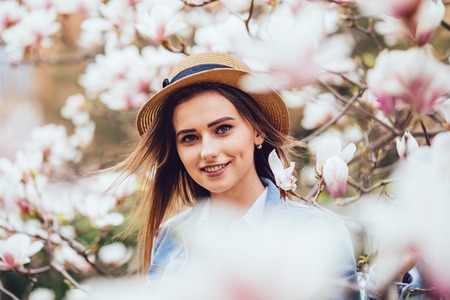 Outdoor portrait of a young beautiful woman near magnolia tree with flowers. Girl wearing stylish...