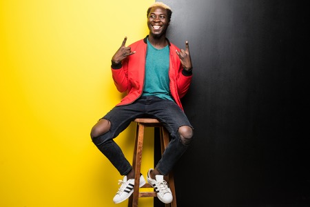 Happy young african man sitting in a chair isolated over color background