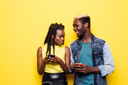 Portrait of a suspicious afro american couple with mobile phone isolated over yellow backgroundの写真素材