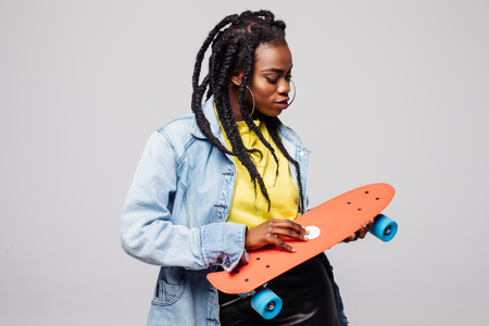 Portrait of happy smiling afro american teenager girl holding skateboard isolated over gray backgroundの写真素材