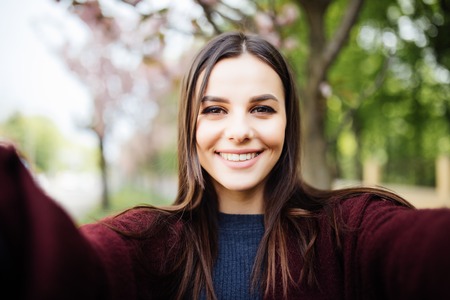 Young woman take selfie near blooming sakura tree from phone outdoorの写真素材