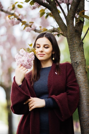 Young pretty woman with sakura flowers in hands near sakura treeの写真素材