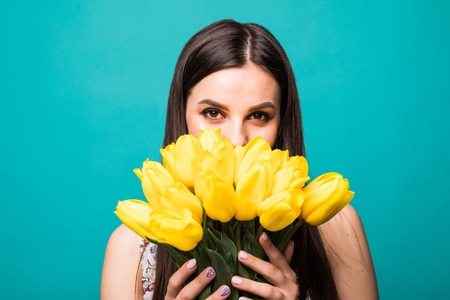 Portrait of joyful young woman in summer dress holding yellow tulips bouquet isolated over blue backgroundの写真素材