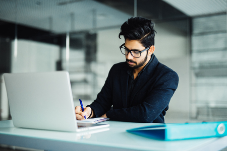 Cheerful young businessman writing in notebook on desk.