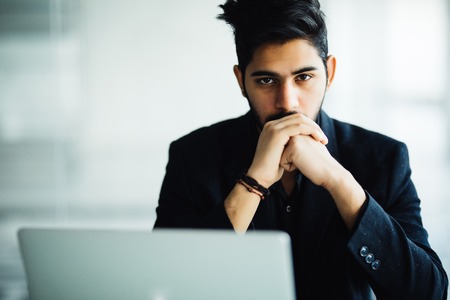Indian thinking Man in glasses working on laptop in officeの写真素材