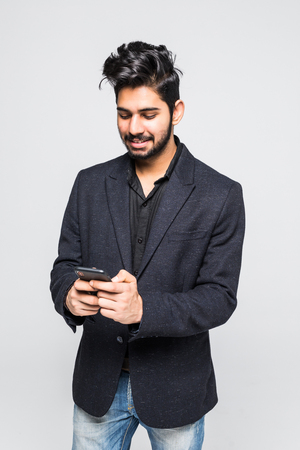 Portrait of handsome casual business Indian man using smartphone, social media concept, standing on plain background with shadow, copy space at side.の写真素材