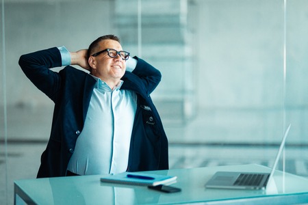 Successful businessman sitting pondering a problem or new idea relaxing back in his chair at the office with his hands behind his headの写真素材