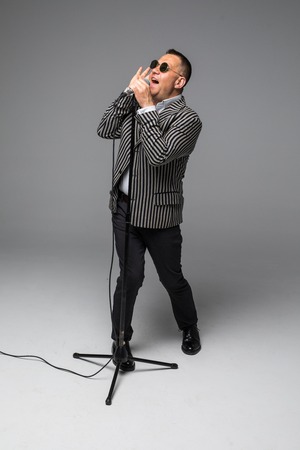 The mid age Showman interviewer with emotions. Young elegant mature man holding microphone against white background.の写真素材