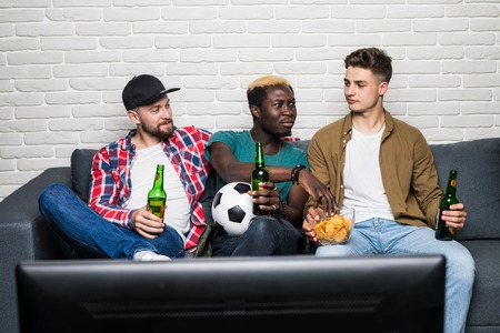 group of exited men sitting together on couch, watching television holding beers, screaming