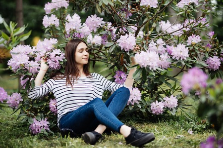 Young smiling beautiful brunette woman sitting near purple flower outdoors