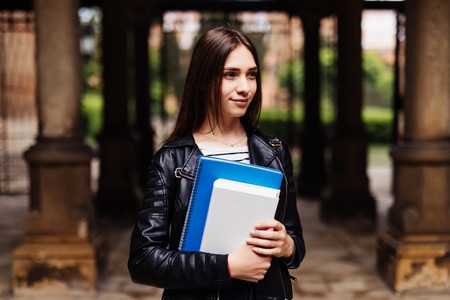 Happy young woman student with backpack holding books and walking outdoorsの写真素材