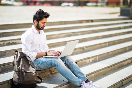 Handsome young manager working on laptop while sitting outdoors on the stairs.の写真素材
