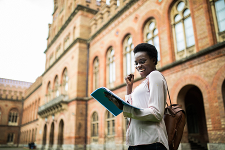 Close up image of a young female student doing assignments in library. Afro american woman taking notes from textbooks.の写真素材