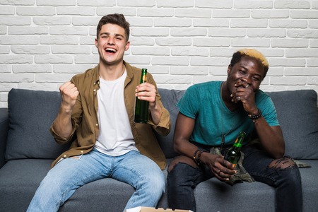 Young two men support their team with different emotions on sofa at homeの写真素材