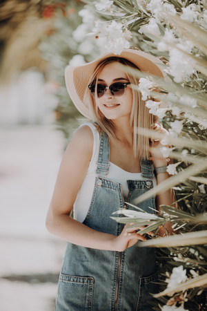 Outdoor portrait of beautiful woman in straw hat near white Blooming tree on the streetの写真素材