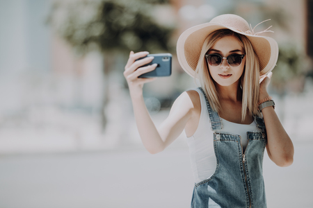 Young attractive playful tourist is making selfie on the phone , wearing hat, sunglasses.の写真素材