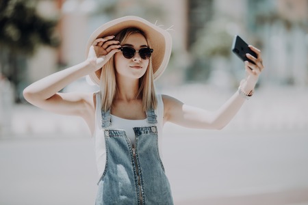 Young attractive playful tourist is making selfie on the phone , wearing hat, sunglasses.の写真素材