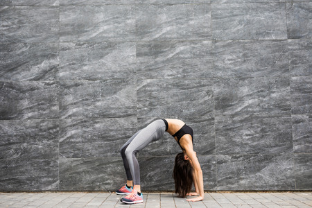 Young sexy woman fitness body stretching and make yoga exercises ootdoors on color city wall