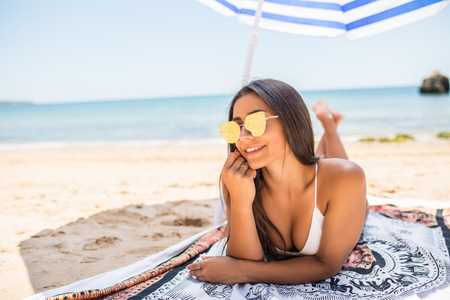 Photo of pretty girl in swimsuit lying on sandy beach with colorful beach umbrella near byの写真素材